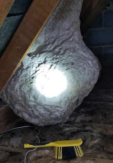 A wasp nest with a hand brush for scale. The central white spot is the beam of a rather bright torch shining on the nest